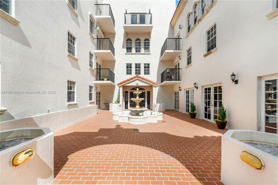 Front view of a multi-story building with balconies and a central fountain in the courtyard.
