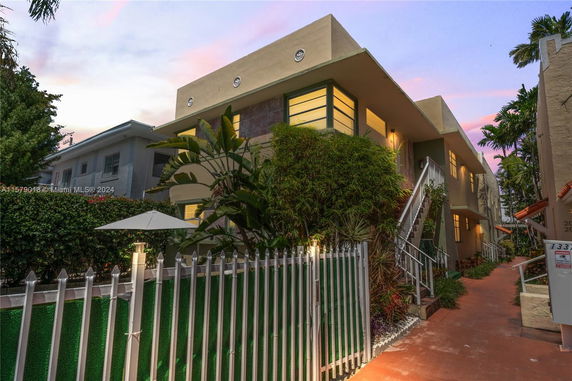Front view of a two-story residential building with exterior stairs and a fenced garden area.
