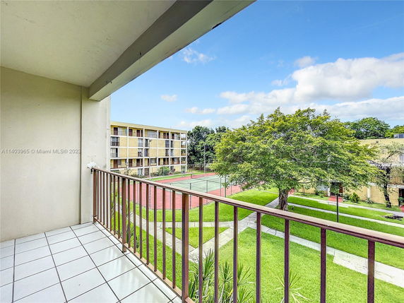 View from a balcony overlooking a courtyard with trees and a tennis court.