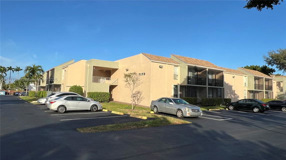 Front view of an apartment building with a parking area in the foreground.