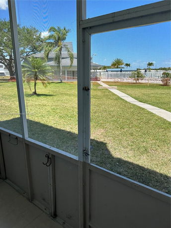View of a lawn area with palm trees and a building in the background seen through a window.