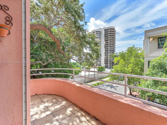 Balcony view overlooking a street with a tall building and trees.