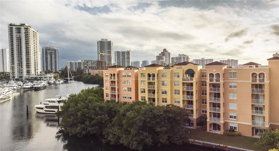 View of a waterfront apartment complex with nearby high-rise buildings and boats docked along a canal.