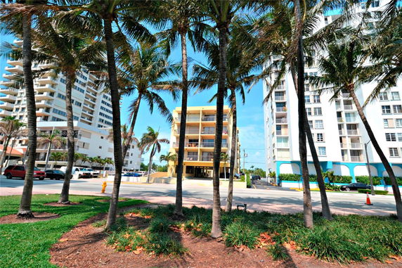 Front view of a multi-story building with balconies, surrounded by palm trees.