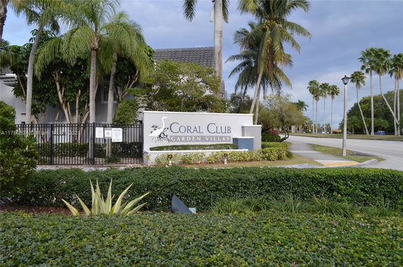 Entrance view of Coral Club Garden Villas with sign and surrounding palm trees.