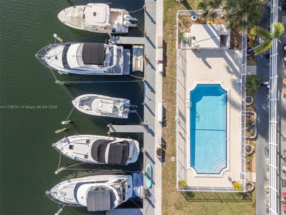 Aerial view of a swimming pool adjacent to a marina with several boats docked.