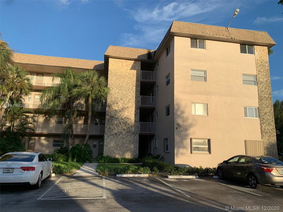 Front view of a multi-story residential building with balconies and a parking area.