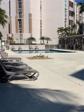 Outdoor pool area with lounge chairs and a multi-story building in the background.