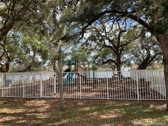 Playground with slides and benches surrounded by a fence and trees.