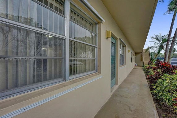 Exterior view of a building corridor with windows and a door, adjacent to a small garden with plants.