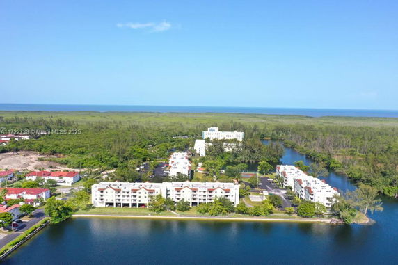 Aerial panoramic view of a cluster of multi-story residential buildings surrounded by greenery and water.