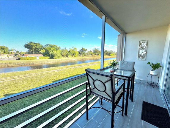 Balcony view of a grassy area with a small pond and distant houses.