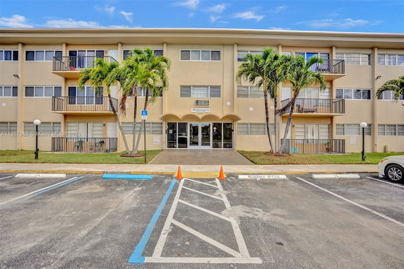 Front view of a three-story building with multiple balconies and palm trees.