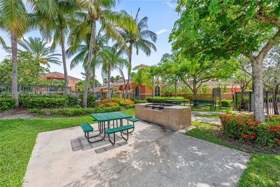 Outdoor area with benches, a barbecue grill, and surrounding palm trees.