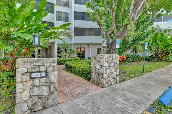 Front view of a multi-story residential building with stone pillars and landscaped entrance.