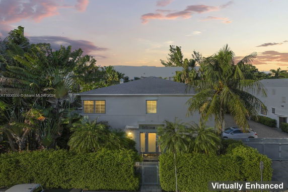 Front view of a two-story house with a flat roof and surrounded by tall palm trees.
