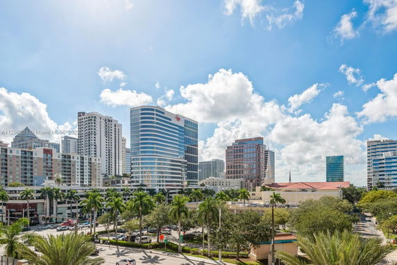 Cityscape view with tall buildings and palm trees under a blue sky.