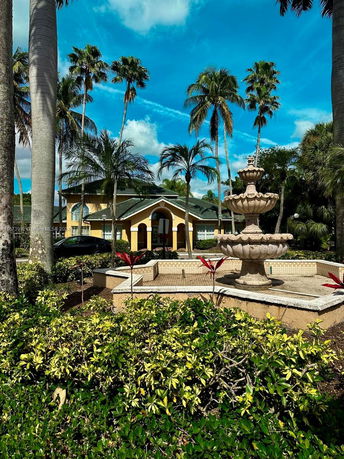 Front view of a house with tall palm trees and a large fountain in the garden.