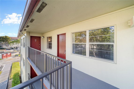 Exterior hallway of a building with red doors and view of surrounding area.