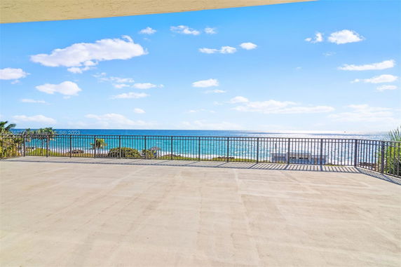 Outdoor terrace with a metal railing overlooking the ocean and distant shore.