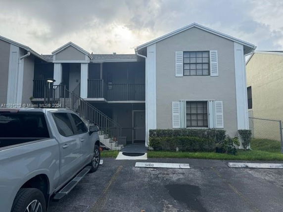 Front view of a two-story residential building with a covered staircase and parking space in front.