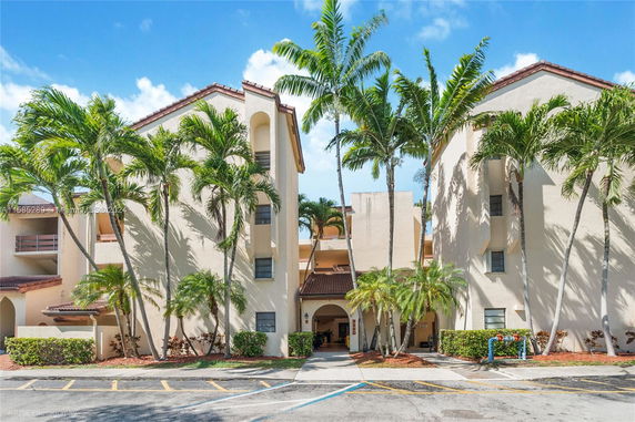Front view of a multi-story building with palm trees and a tiled roof.
