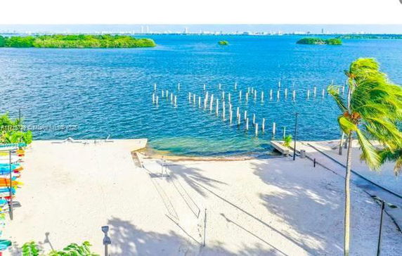 Panoramic view of a beach with a dock extending into the water and islands in the distance.