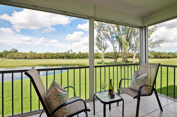 View from a balcony overlooking a grassy area and a pond with trees in the background.