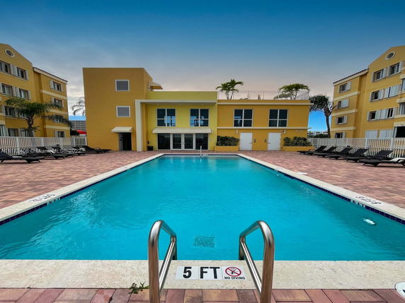 View of an outdoor swimming pool with a yellow building in the background.