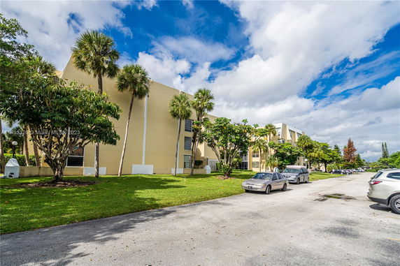 Front view of a multi-story building with palm trees and parked cars.