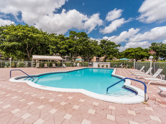 Outdoor swimming pool with lounge chairs and trees in the background.