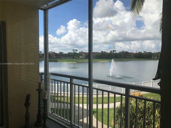 View of a lake with a fountain and houses in the background, seen from a screened balcony.