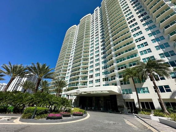 Front view of a high-rise residential building with numerous balconies and a covered entrance.