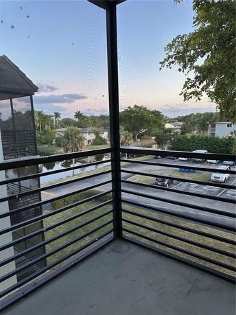 View from a balcony overlooking a parking area and residential neighborhood with trees.