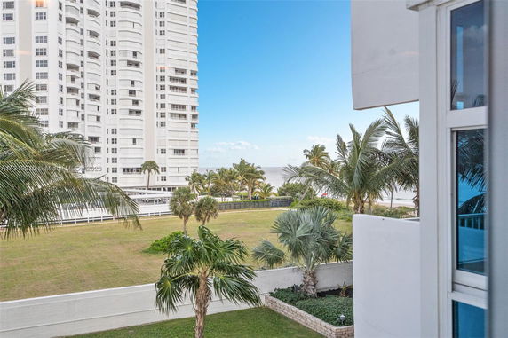 View of a high-rise building with palm trees and the ocean in the background.