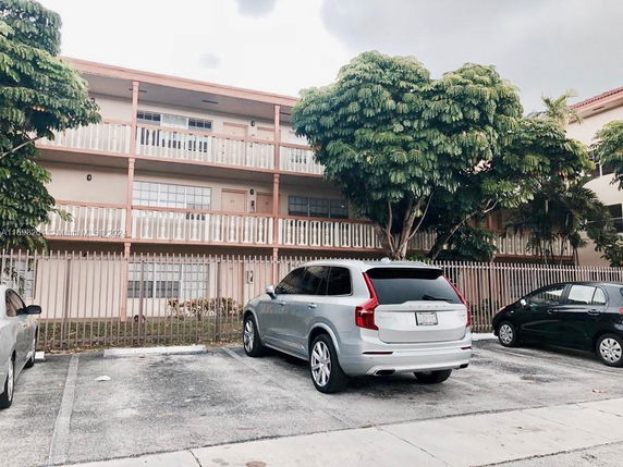 Outdoor parking area in front of a multi-story residential building with balcony railings.