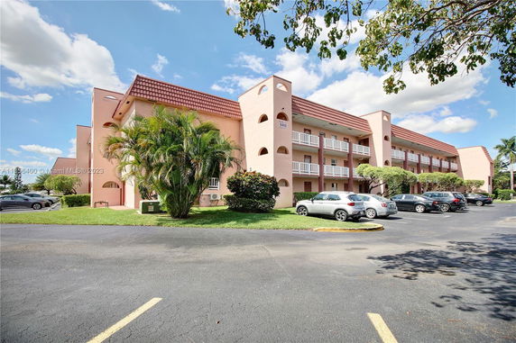 Front view of a multi-story apartment building with balconies and parking area.