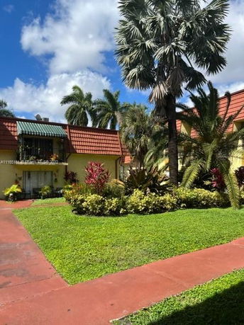 Front view of a building with red-tiled roof and balcony, surrounded by palm trees and a garden area.
