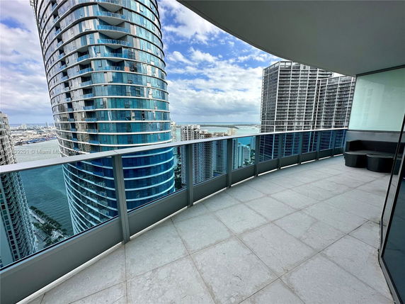 View from a balcony overlooking tall modern buildings and a large body of water.