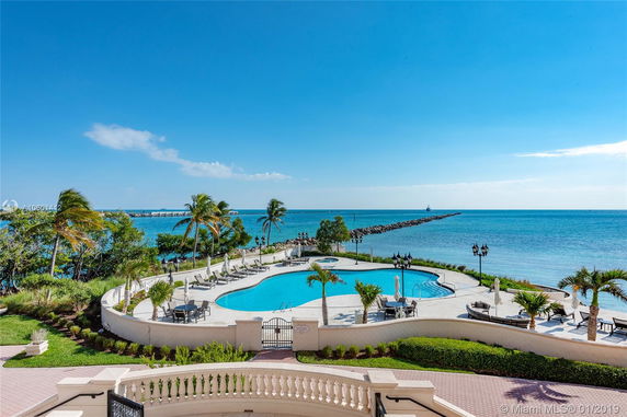 Overlooking view of a pool area with surrounding ocean and palm trees.
