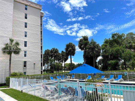 Outdoor area with a swimming pool, surrounded by a white fence, near a multi-story building.