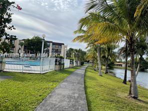 Outdoor swimming pool area surrounded by a path and palm trees near a waterfront.