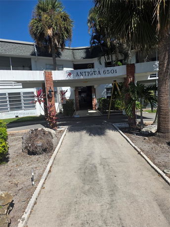Front view of a building with palm trees and a curved entrance.