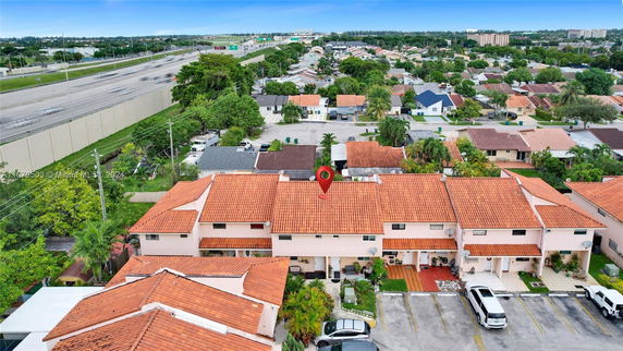 Aerial view of a row of houses with tile roofs, adjacent to a highway, and surrounded by a residential neighborhood.
