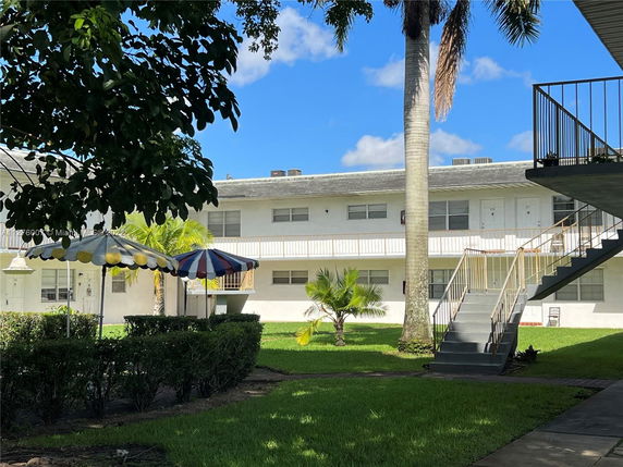 Front view of a two-story apartment building with external staircases and canopies in a grassy courtyard.