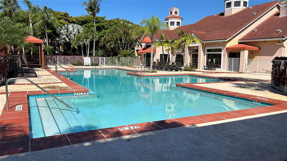 Swimming pool area with adjacent building featuring red-tiled roof and outdoor seating.