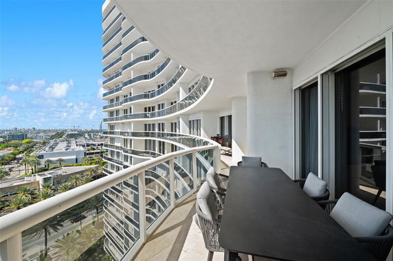 Curved balcony view of a high-rise building with glass railings overlooking other buildings and palm trees.