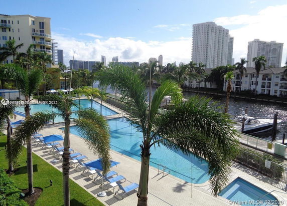 Outdoor swimming pool area with deck chairs and palm trees.