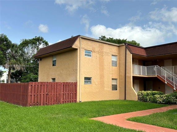 Side view of a two-story residential building with a fenced yard.