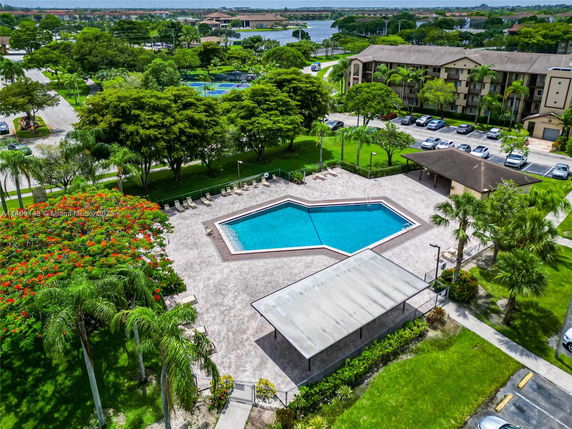 Aerial view of a swimming pool with surrounding greenery and adjacent apartment buildings.
